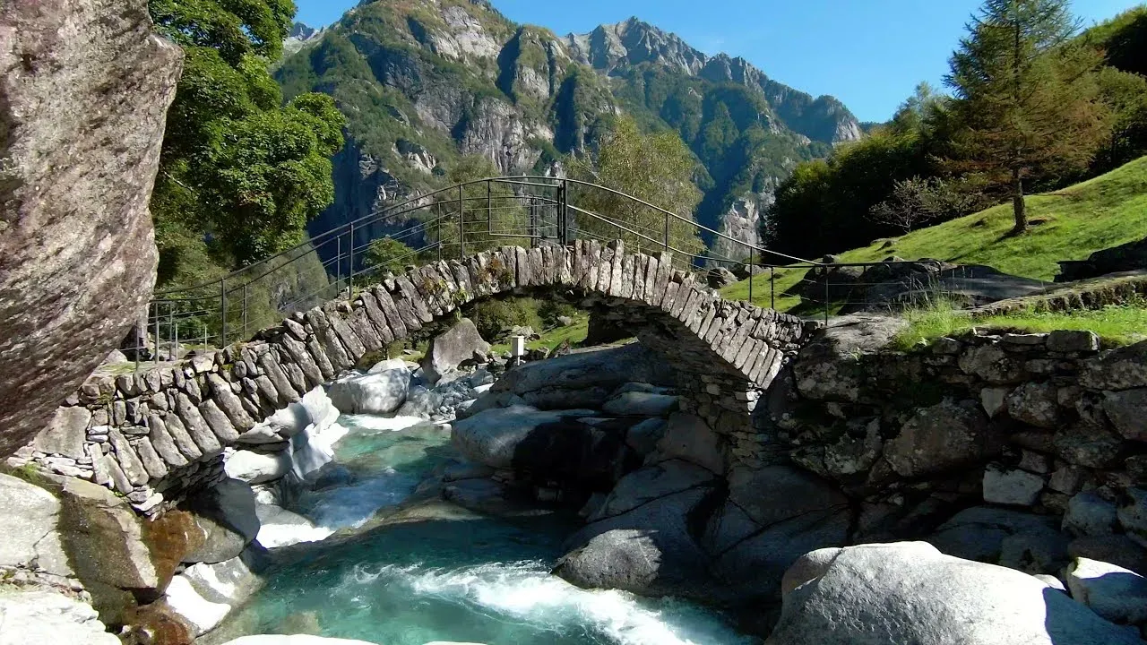 Bogenbrücke aus Trockenmauerwerk über den Bach bei Puntid im Val Calnègia, dahinter die Felswände des Tals