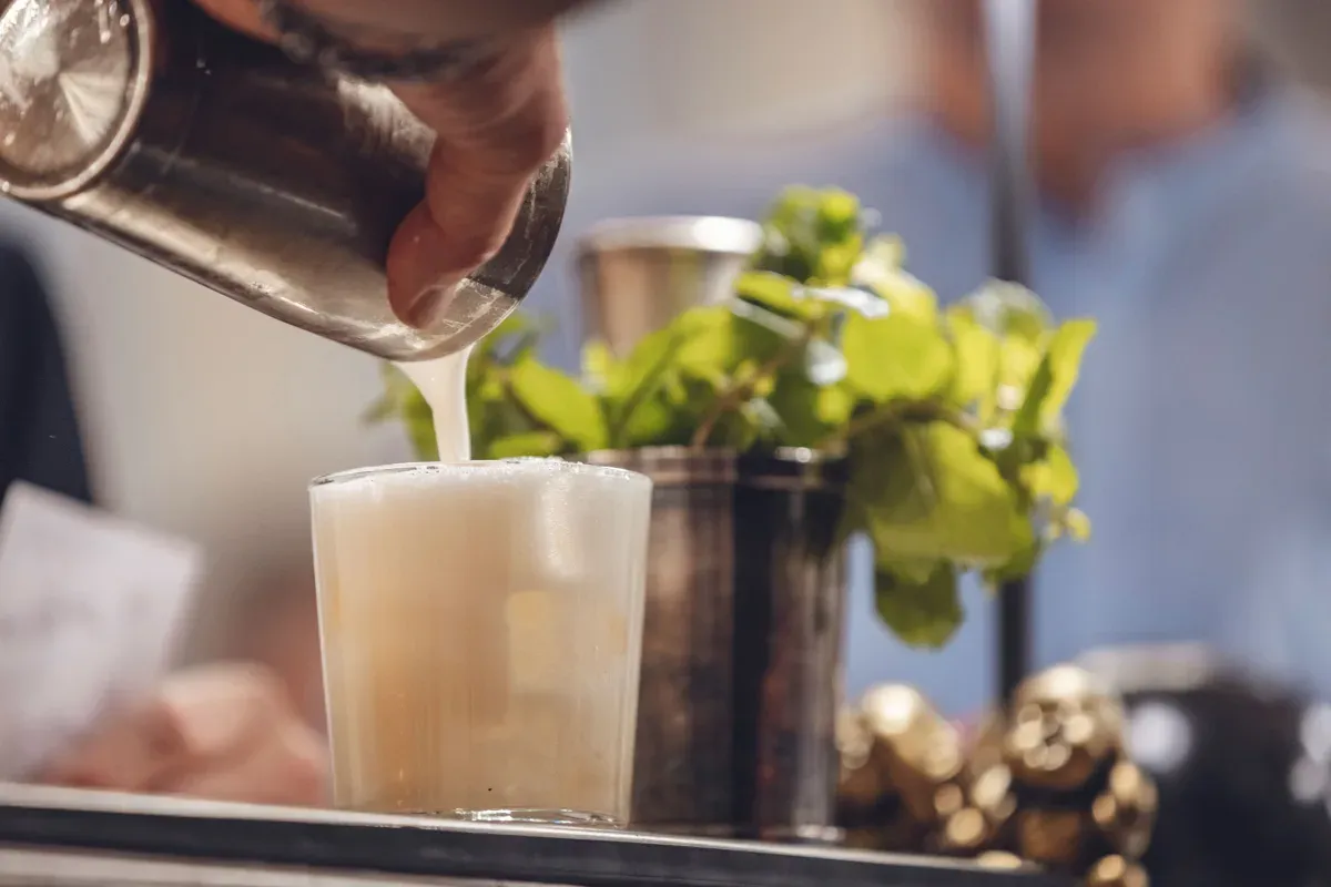 Ein milchiger Drink wird aus dem Shaker in ein Glas gegossen